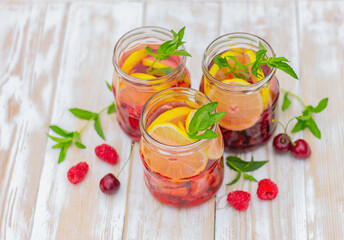 drink from lemon, berries and mint in glass jars on a white wooden table. summer refreshing lemonade.
