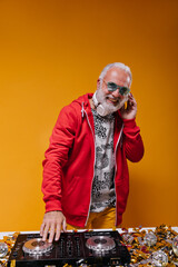 Man in red jacket and headphones plays music with dj controller. Smiling adult guy in blue...