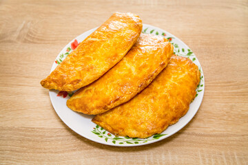 Baked puff pastry with delicious yellow cheese on a round plate on a wooden board background. Bakery products national traditional dishes and pastries.