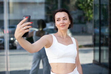 stylish adult woman takes selfie portrait on phone while standing in the middle of the urban street