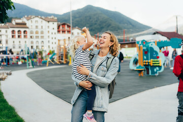 Happy laughing mother holding her little daughter in her arms is walking in the city.
