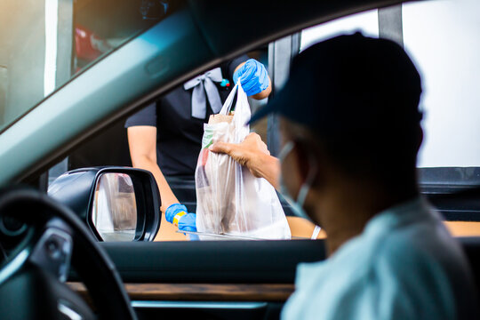 Selective focus to hand of staff wearing medical glove and mask  to handed a food to customer. Drive thru and take away concept.