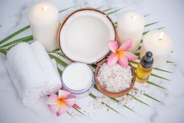 Fototapeta na wymiar Coconut oil, tropical leaves and fresh coconuts. Spa coconut products on light wooden background. Spa still life of organic cosmetics with coconuts on a light wooden background, body care concept.