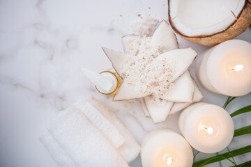 Obraz na płótnie Canvas Coconut oil, tropical leaves and fresh coconuts. Spa coconut products on light wooden background. Spa still life of organic cosmetics with coconuts on a light wooden background, body care concept.