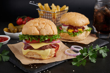 Two mouth-watering, Homemade hamburger with fresh vegetables and cheese lettuce and mayonnaise served, French fries on pieces of brown paper on black stone table . concept of fast food and junk food