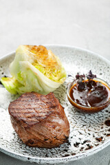filet mignon on ceramic plate closeup on concrete table. meat with grilled cabbage with bbq sauce
