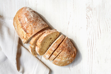 Sliced organic bread ciabatta with vintage linen napkin on white wooden background. Top view of homemade ciabatta. Flat lay.