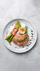 grilled steak with asparagus and rosemary leaf in plate top view on concrete background with copy space