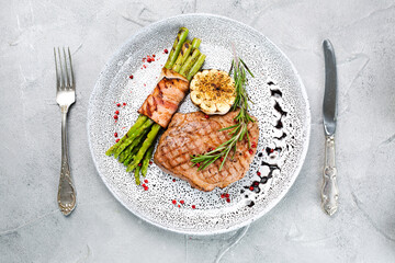 grilled steak with asparagus and rosemary leaf in plate top view on concrete background with copy space