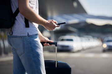 Man holding smartphone and using mobile app against a row of taxi cars. Themes modern technology,...