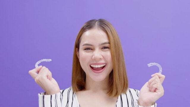 Young smiling woman holding invisalign braces in studio, dental healthcare and Orthodontic concept..