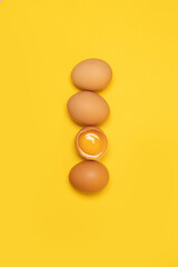 Tasty brown chicken eggs and one broken egg with yolk on yellow background. Minimal Easter concept idea.