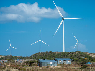 Dramatic image of wind turbines in the wind, with small poor Caribbean village in foreground.
