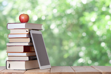 stack of books with red apple and digital tablet on the nature blurred background with bokeh lights...