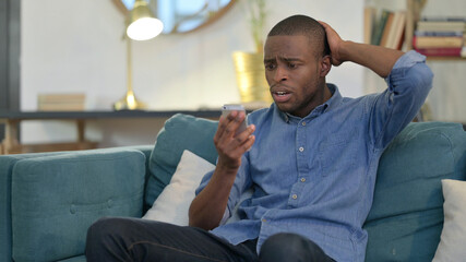 Young African Man Reacting to Loss on Smartphone on Sofa 