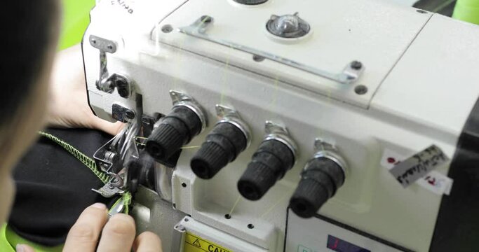 Four-thread overlock sewing machine. Female hands, working on tailoring. Automatic industrial sewing machine for textiles. Production of knitwear.