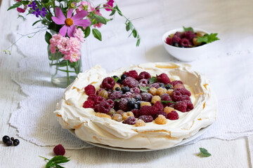 Pavlova cake with cream and berries and a bouquet of flowers on a light background.