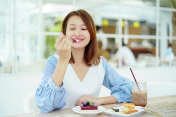 A beautiful Asian portrait is taking a spoonful of cakes on the table and eating them with happy eyes and expressions in the bakery.