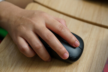 Close Up A woman's hand is holding on a black mouse to operate the computer.