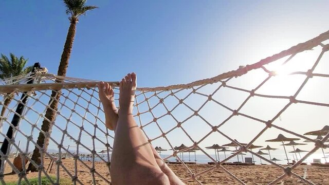 woman relaxing on hammock. Low angle view. Beautiful female feet relaxing in a hammock on the beach against the background of the sky