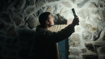 Young handsome tourist or archaeologist with a flashlight examining the walls inside a historic castle