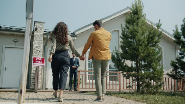Couple man and woman are walking to beautiful new house for sale and talking to real estate agent discussing deal. Buying property and people concept.
