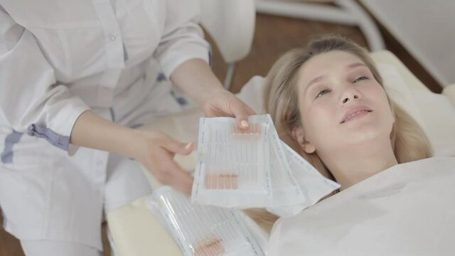Cropped top image of face of pretty blond Caucasian woman, ready to get beauty injections, skin treatment, lying on the couch in cosmetology clinic. Hands of beautician holding set of syringes