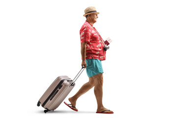 Full length profile shot of a mature male tourist holding a passport and pulling a suitcase