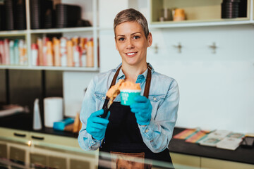 Young and happy saleswoman in black apron selling handmade ice cream at the counter of the pastry shop.