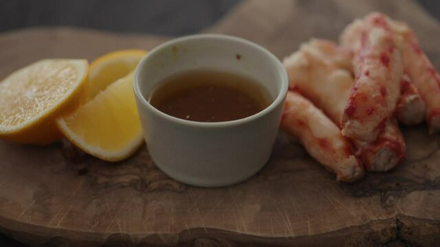 Slow motion gimbal shot of crab leg meat on a olive board with sweet lemon and dip sauce
