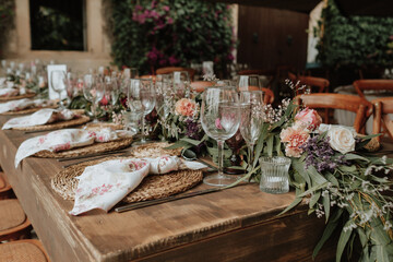 Close-up of a rustic wedding setting table with flowers and colorful glasses on a wooden table