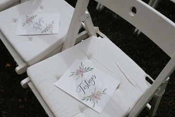 White wooden chair prepared for the wedding ceremony with a card saying where to sit to the testigos