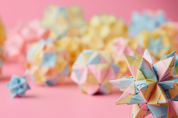 Set of multicolor handmade modular origami balls or Kusudama Isolated on pink background. Visual art, geometry, art of paper folding, paper crafts. Close up, selective focus, copy space.