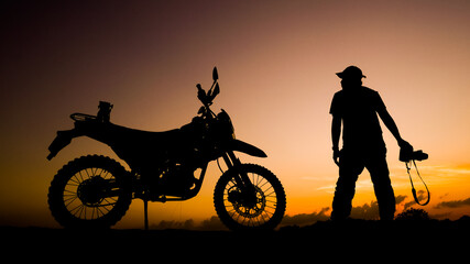 Silhouette photographer adventures with a motorcycle off-road or motocross in the evening. travel...