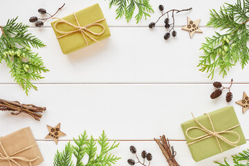 Christmas frame made of gift boxes, conifer branches and natural decorations on white wooden background