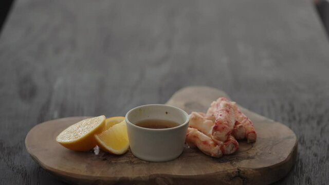 Slow motion gimbal shot of crab leg meat on a olive board with sweet lemon and dip sauce