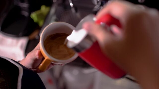 closeup barista pour milk into a cup in a cafe making latte art