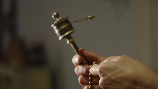 Tibetan monk praying with the mantra wheel and the mala.
The close-up shot shows his hands in slow motion, as he counts the prayers and the pinwheel rotates in slow motion.