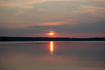 Evening on the lake in summer in July. The sun and sky are reflected on the calm surface of the...