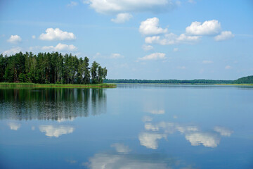 Obraz na płótnie Canvas Blue sky and blue water. White clouds are reflected in the forest lake. Horizon.