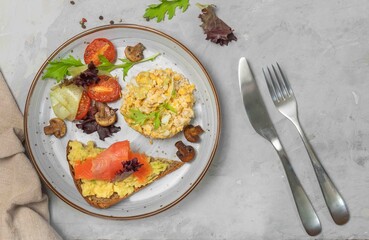 Breakfast with scrambled eggs, salad and toast with salmon, avocado and parmesan. Close-up on a gray background, horizontal