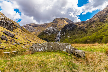 Fototapeta na wymiar A view past a rock towards the Steall Waterfall in Glen Nevis, Scotland on a summers day