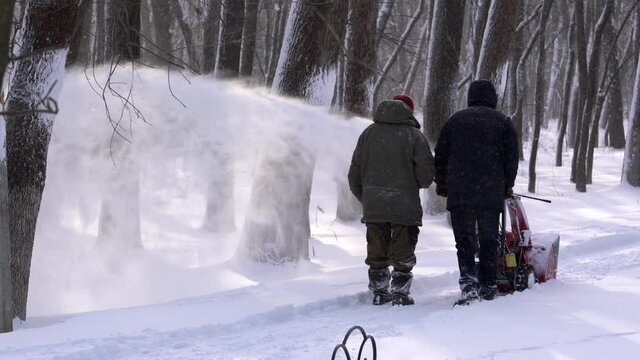 Men remove snow in the park with a snow blower