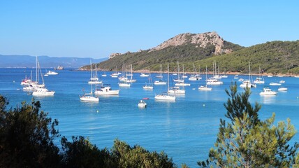 Fototapeta premium Paysage de côte avec des bateaux au mouillage dans l’eau bleu turquoise de la mer Méditerranée, baie Notre-Dame sur l’île de Porquerolles, dans le Var (France)