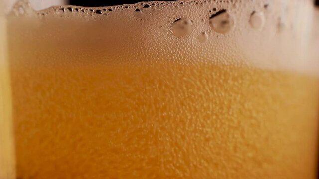Extreme macro footage through a transparent glass of bubbles within foam formed in cold chilled beer due to pouring. Abstract texture in a alcoholic refreshment beverage