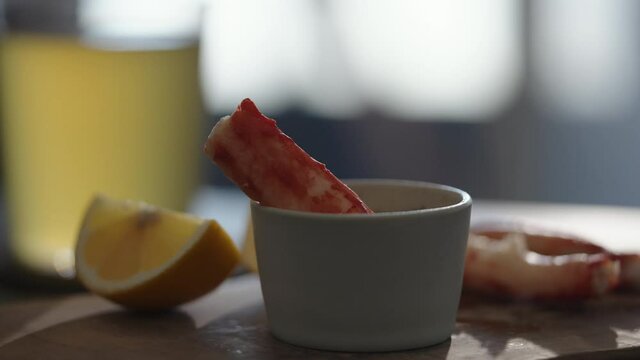 Slow motion gimbal shot of crab leg meat on a olive board with sweet lemon and dip sauce on concrete countertop