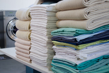 Stack of folded clean sheets, surgical clothes  and industrial iron in an industrial laundry. - obrazy, fototapety, plakaty