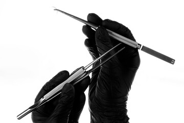 doctor's hands in black gloves with a needle holder and dental tweezers on a white background....
