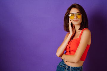 Beautiful young woman in a red top, skirt and yellow glasses posing on a purple background. Beauty and positive concept.