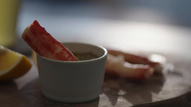 Slow motion gimbal shot of crab leg meat on a olive board with sweet lemon and dip sauce on concrete countertop